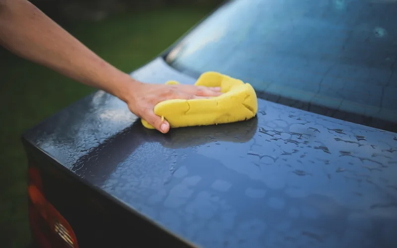 Hand washing a car hood with a yellow sponge