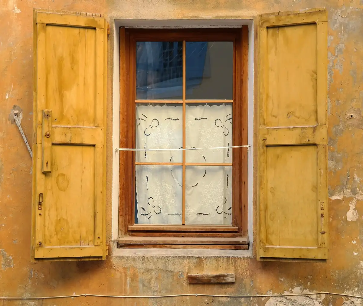 House window with yellow wooden shutters and lace curtains