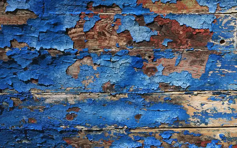 Layers of blue paint flaking off weathered wooden boards