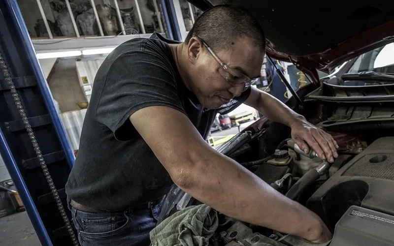 Mechanic leaning over an open car hood working in a repair shop