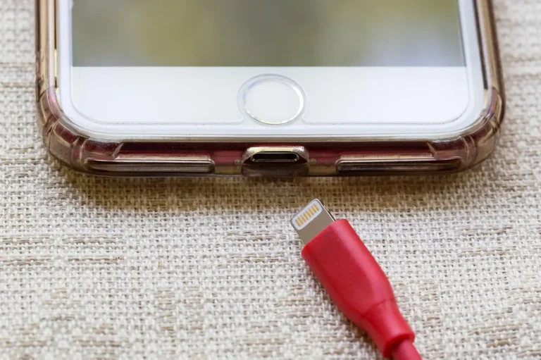 Smartphone with a red Lightning cable about to be plugged into its charging port