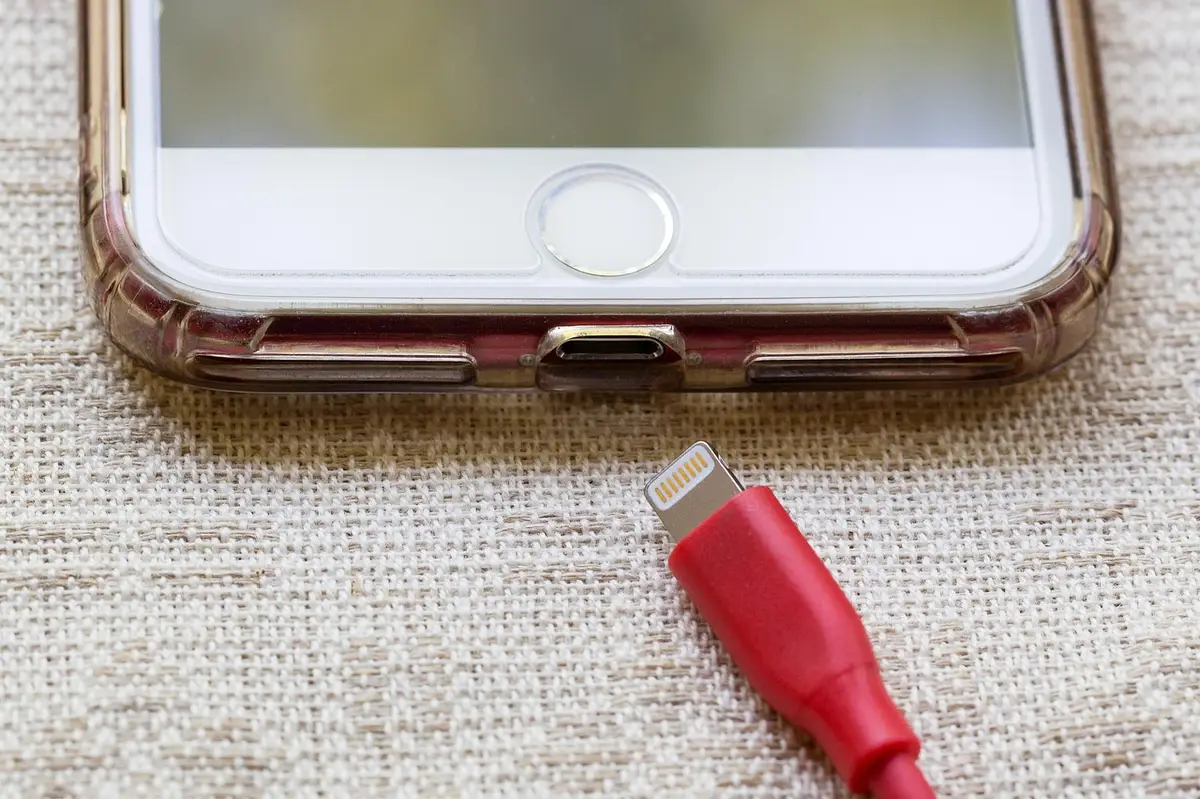 Smartphone with a red Lightning cable about to be plugged into its charging port