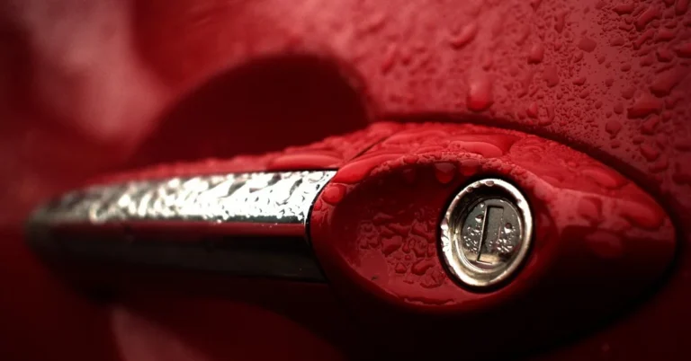 Red car door handle with a keyhole covered in water drops