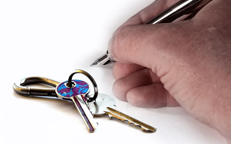Hand signing a document next to a set of keys