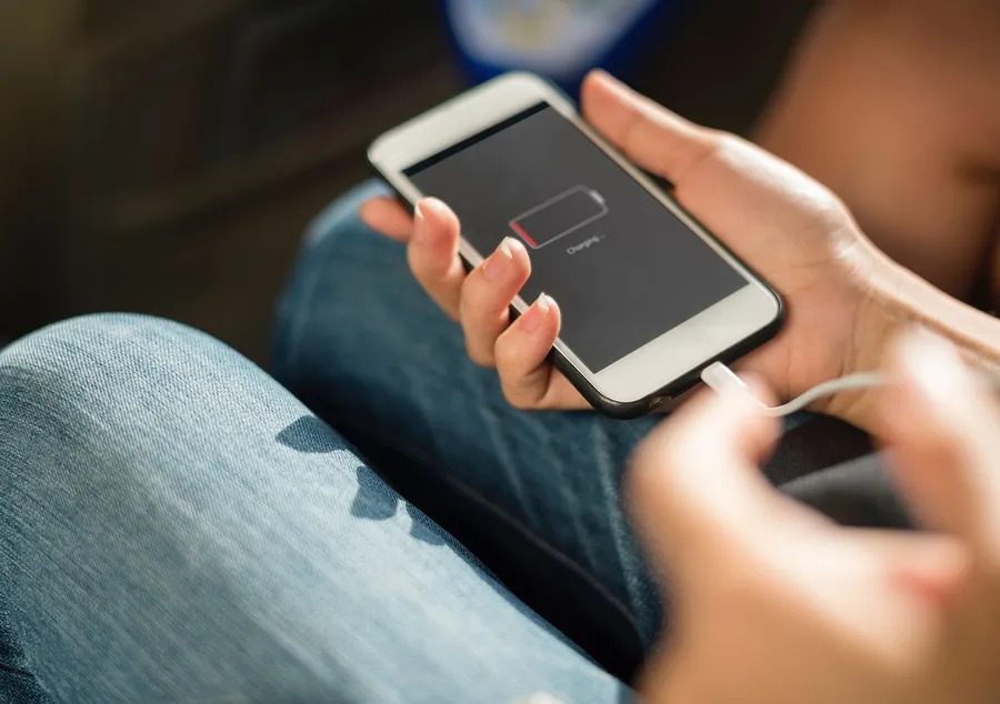Smartphone showing a low battery charging screen held in one hand with a cable attached