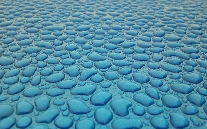 Water beads on a waxed blue car panel