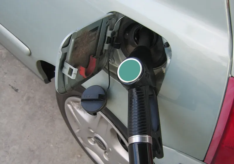Open fuel door on a car with a fuel nozzle inserted and the gas cap hanging beside it