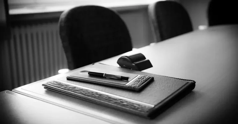 Black fountain pen resting on a leather document folder on a conference table
