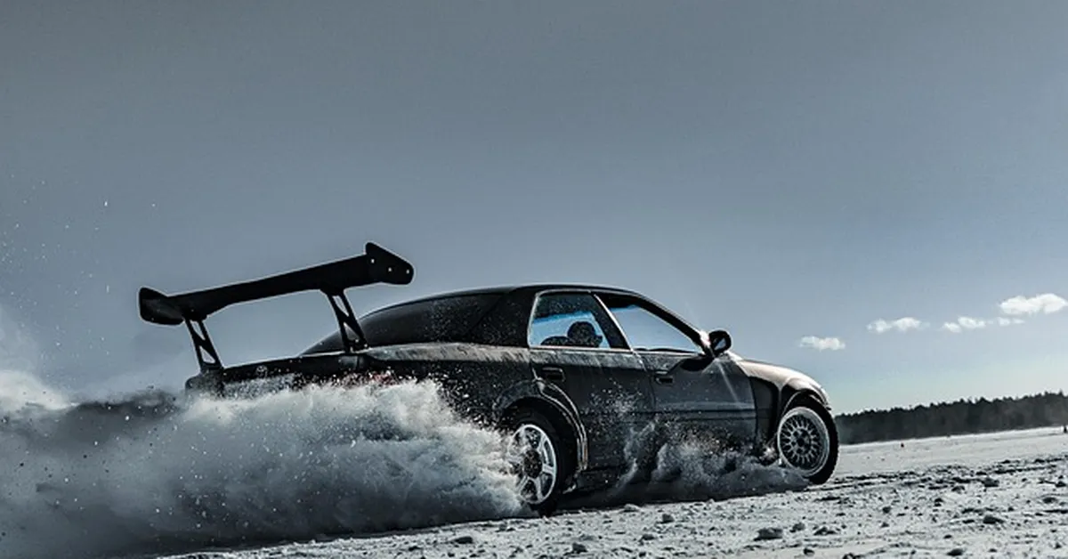 Car with a rear spoiler wing sliding through snow, showing aerodynamic control