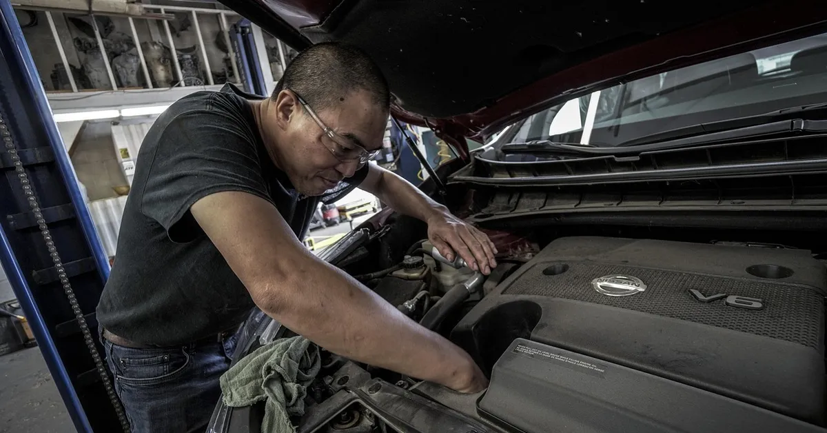 Mechanic inspecting a car engine during a warranty repair visit
