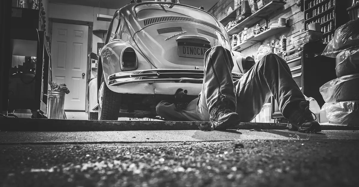 A mechanic working underneath a car on a garage floor during a maintenance repair