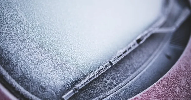Close-up of a frozen car windshield and wiper blade covered in frost