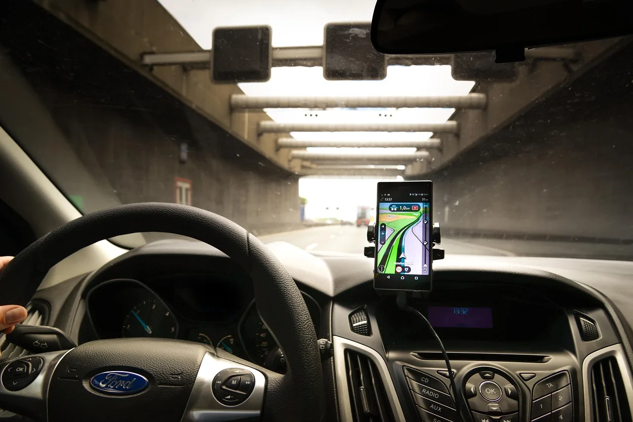 Commuter adjusting a windshield-mounted car phone mount in a compact car at sunrise