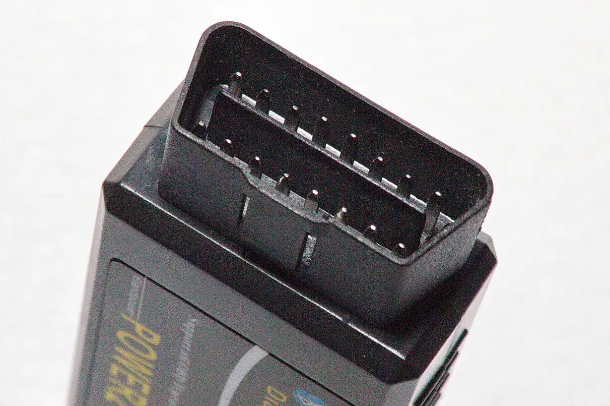 Hand holding an OBD2 scanner near a car dashboard diagnostic port