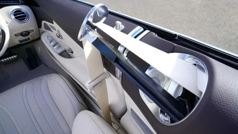 Driver in a car using a seat belt pad, with a few pad styles resting on the passenger seat