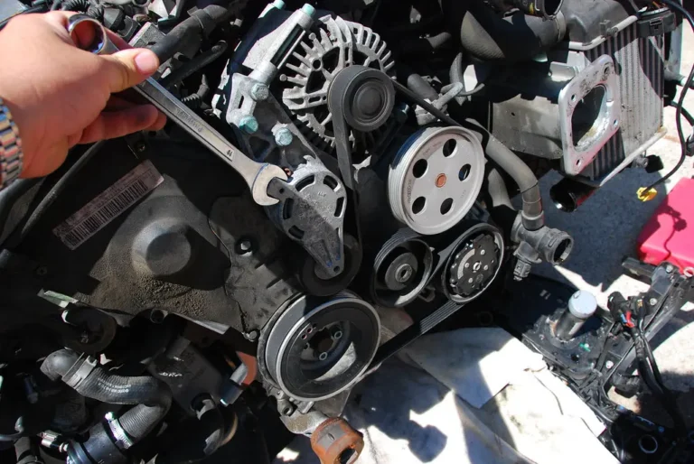Mechanic comparing serpentine belts on a workbench beside an open engine bay
