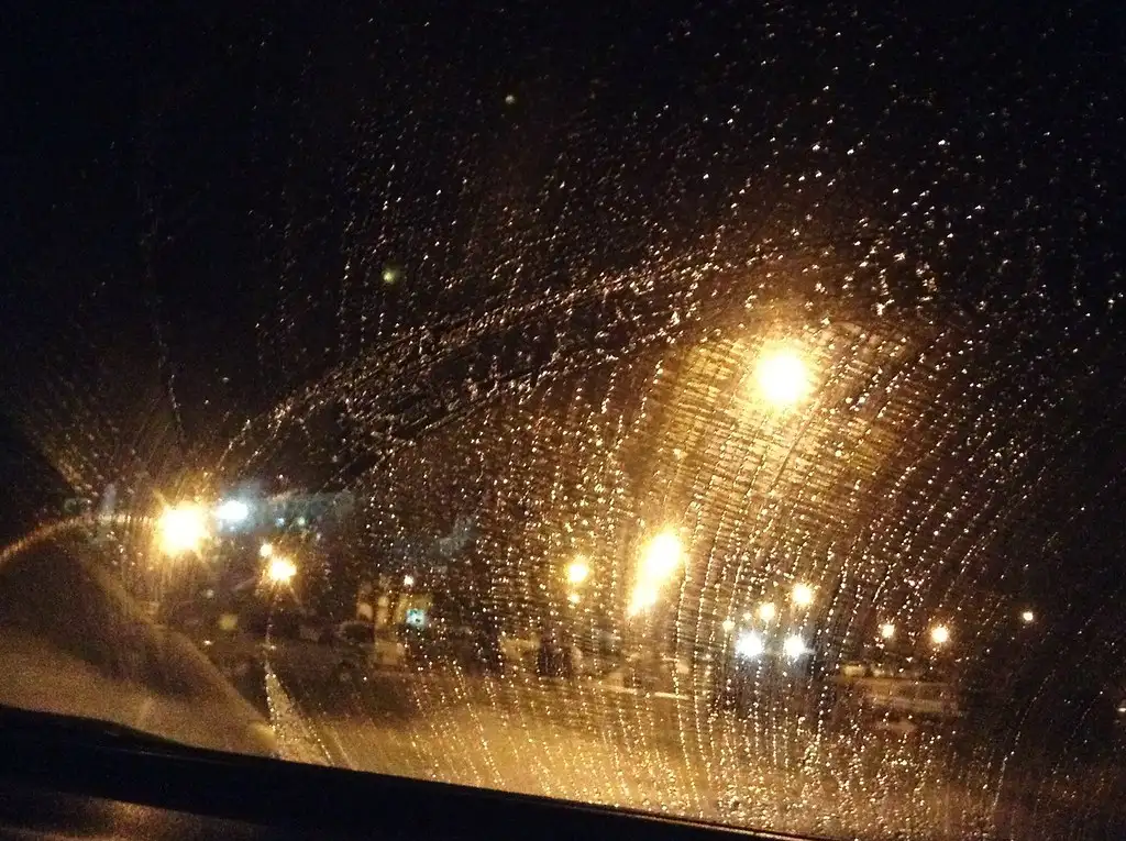 Hand spraying de-icer onto a frozen windshield with a scraper nearby