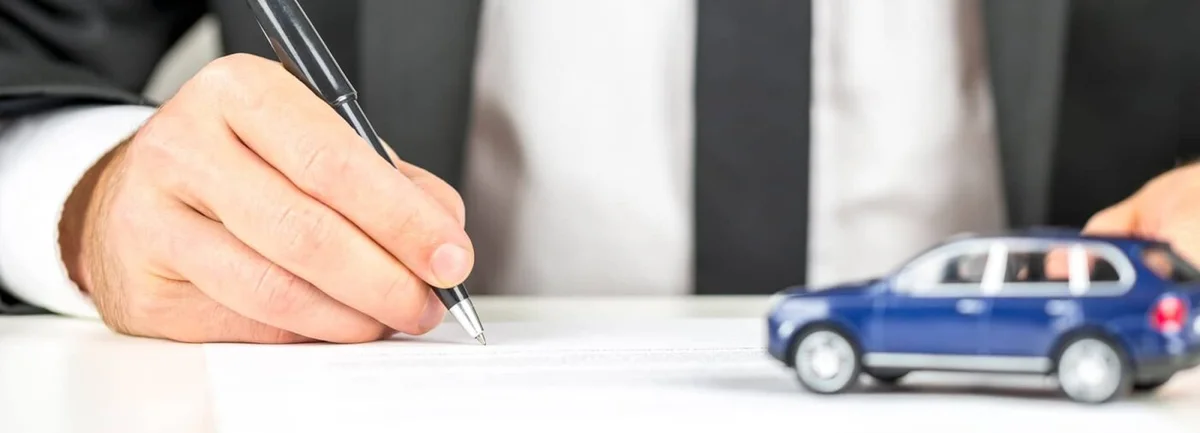 Car buyer signing a purchase contract at a dealership desk next to a model car