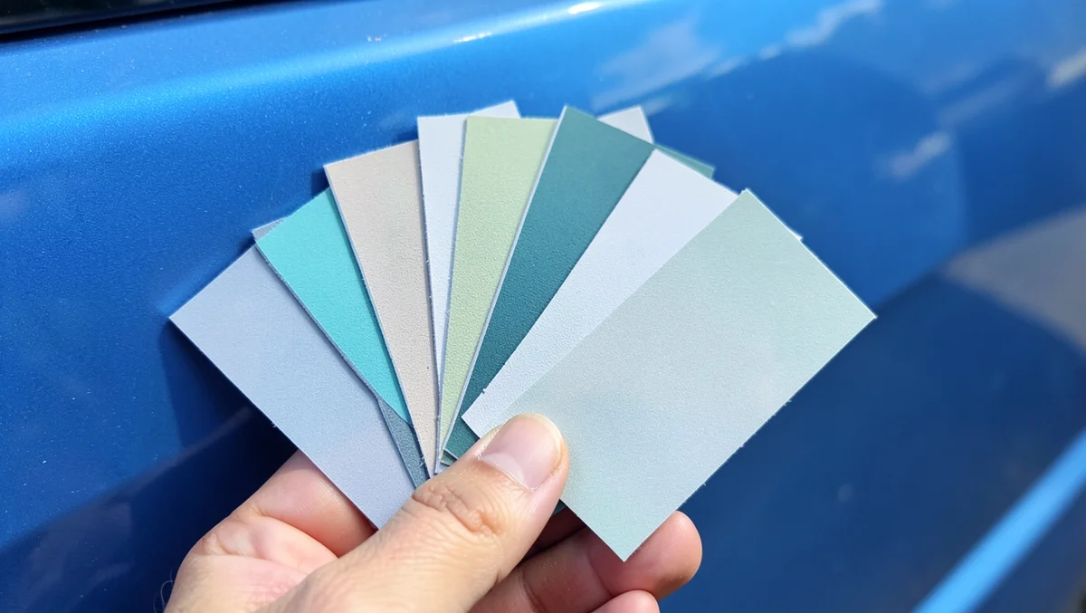 Paint color swatch chips held against a blue car door to check the color match