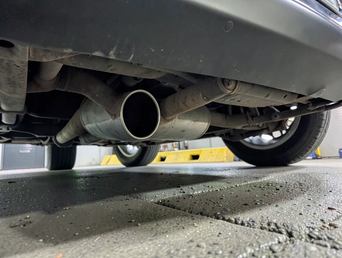 Close-up under a car showing the exhaust pipe and muffler hanging close to the pavement