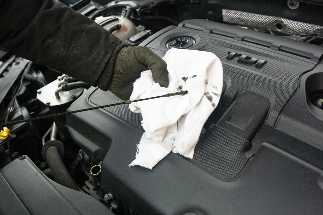 Car owner and mechanic inspect an open hood beside a sedan in daylight.