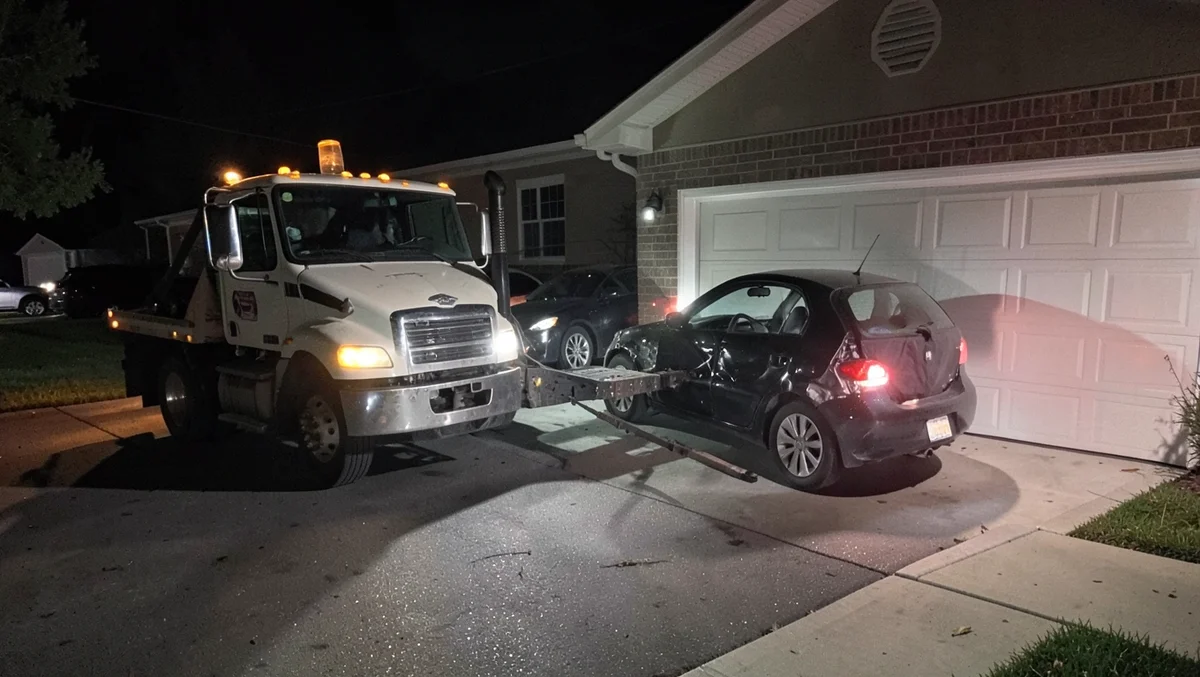 Tow truck repossessing a car from a driveway at night