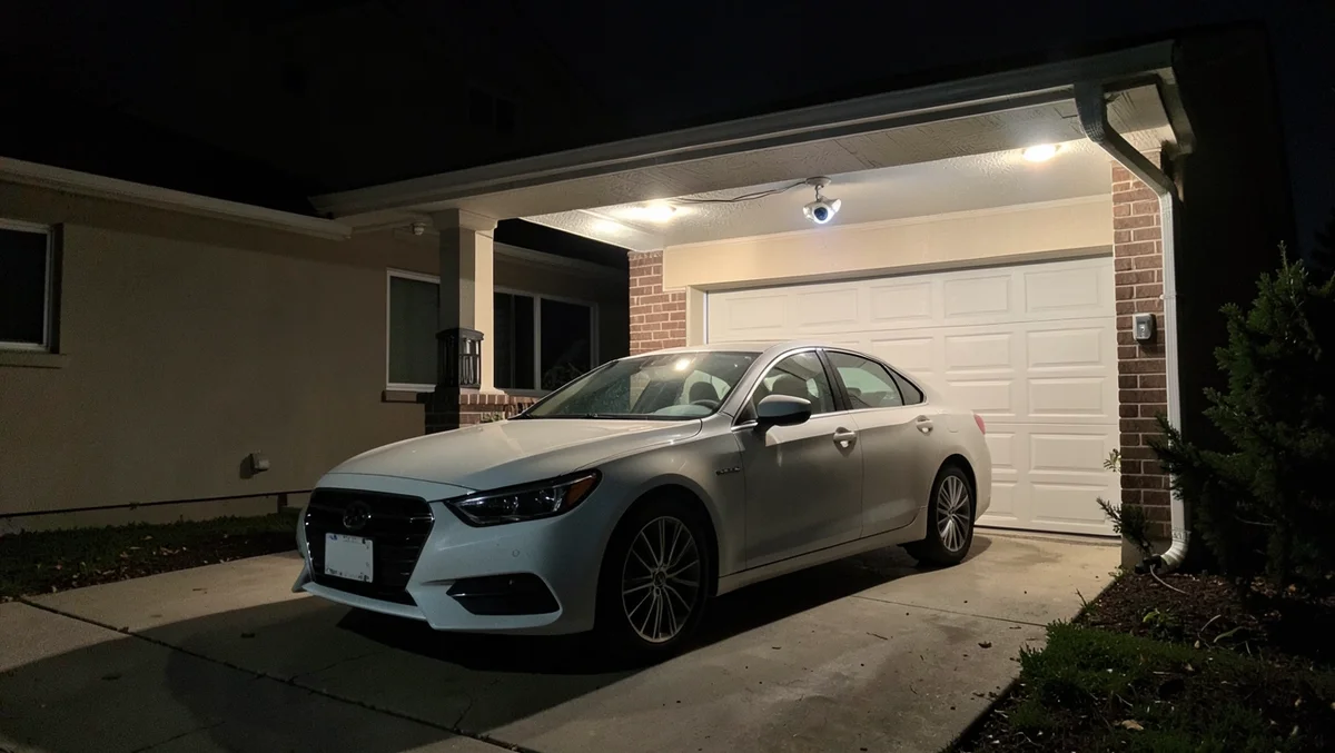 A car parked in a driveway at night under a motion-sensor light with a security camera mounted above the garage