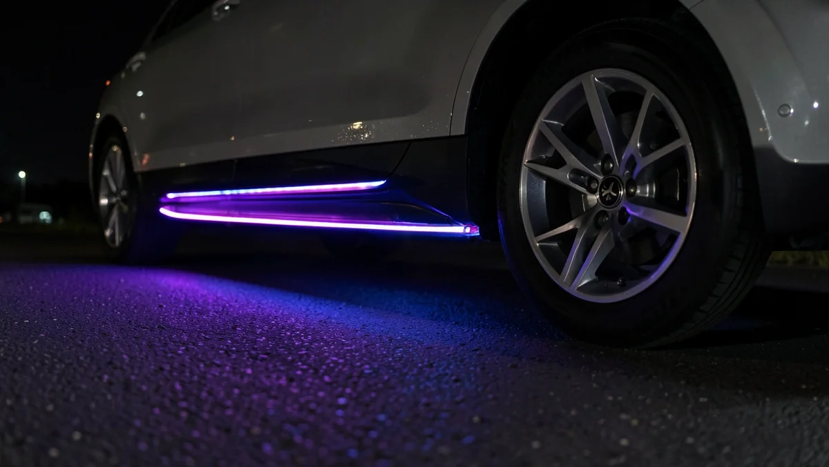 Close-up of colorful purple and blue neon underglow LED lighting glowing beneath a parked car at night