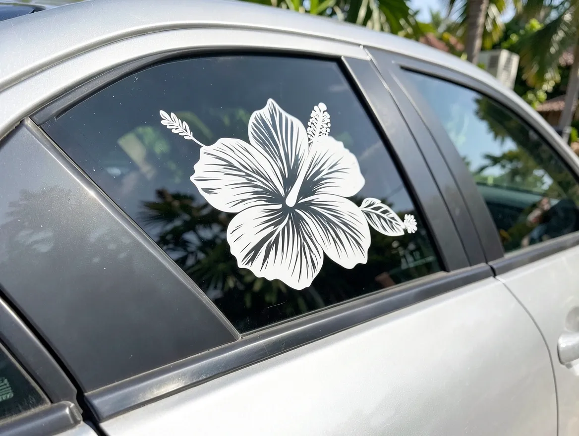White hibiscus flower vinyl decal applied to the rear side window of a silver car parked among palm trees