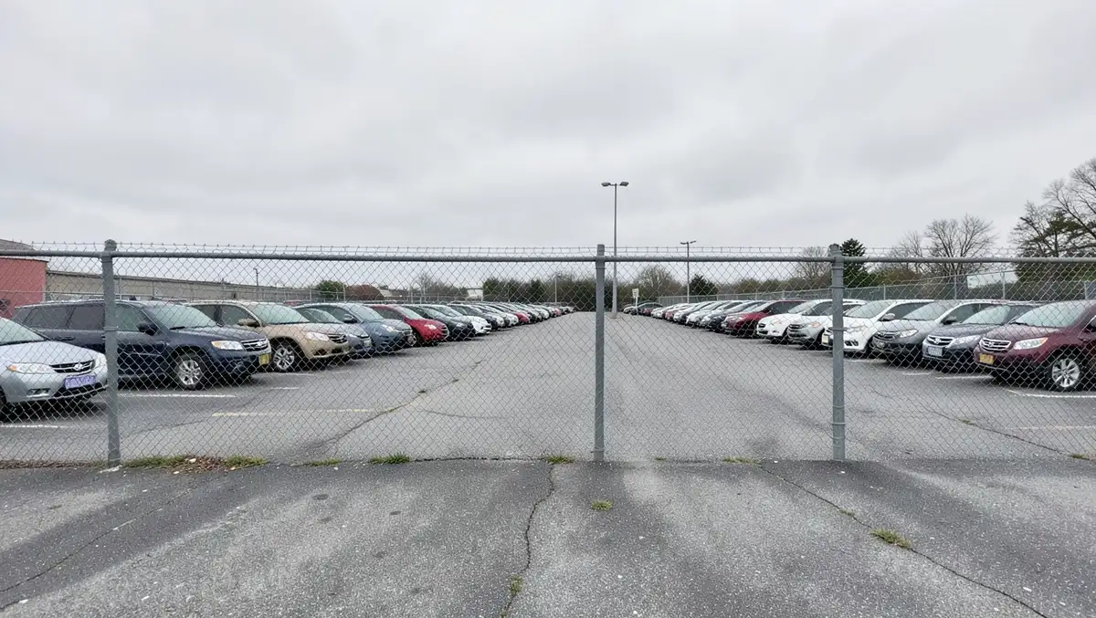 Vehicle impound storage lot with rows of cars parked behind a chain-link fence