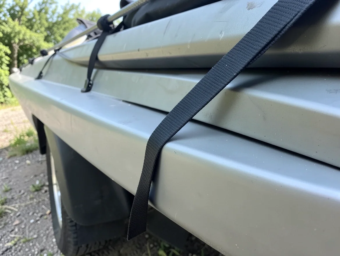 Kayak strapped to a car roof rack showing the tie-down straps running to the front and rear bumpers