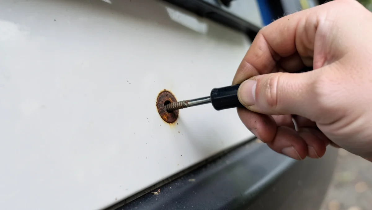 Removing a rusty screw from an old license plate mount with a screwdriver