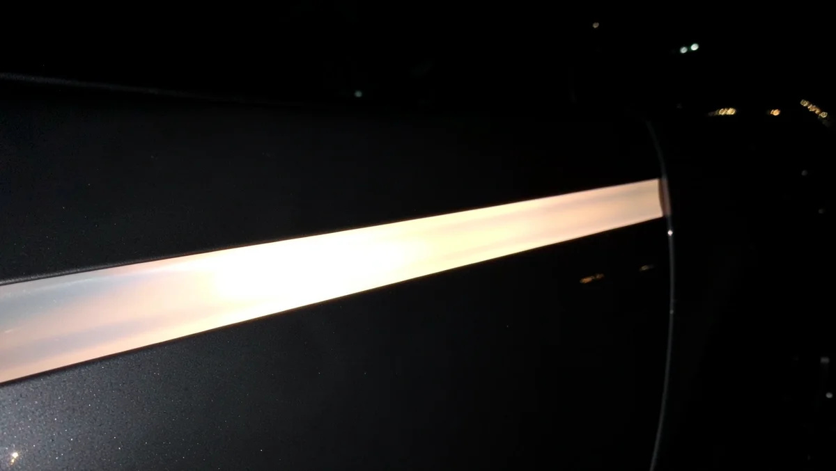 Close-up of retroreflective vinyl strip on a car door glowing brightly when hit by light at night