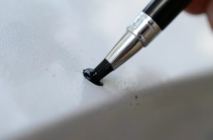 Close-up of a touch-up paint pen brush applying black paint to a small chip on a car panel