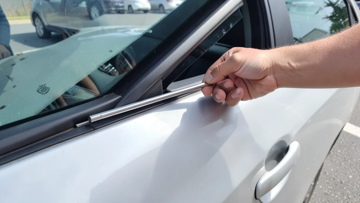 Man using a slim metal rod tool to unlock a car door through the window gap