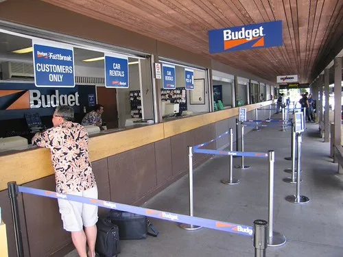 Traveler at a rental car counter comparing reservations with an agent and luggage nearby