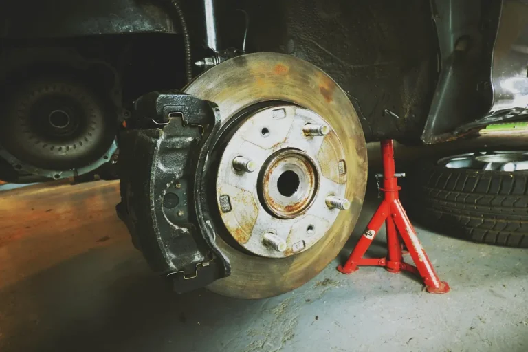 Mechanic and customer review a lifted sedan with exposed brake rotor in an auto repair shop