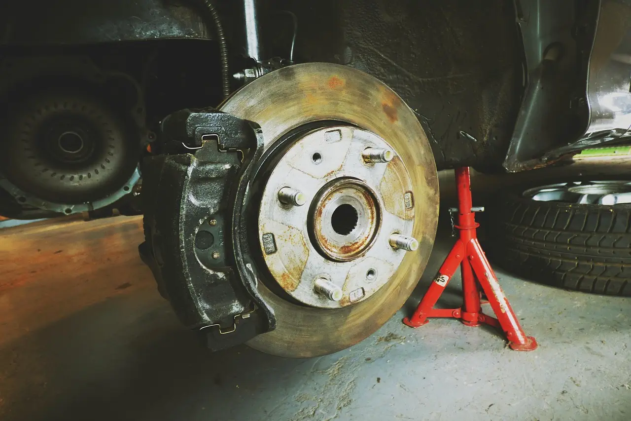 Mechanic and customer review a lifted sedan with exposed brake rotor in an auto repair shop