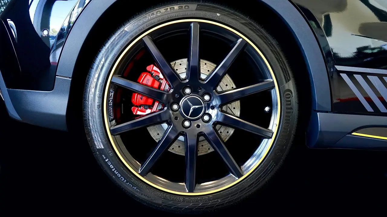 Car detailer cleaning a dusty alloy wheel with brake dust cleaner in natural daylight