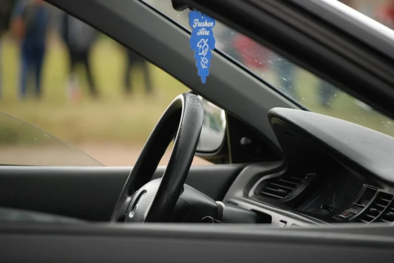 Car interior with a vent clip air freshener, open window, and gym bag on the back seat