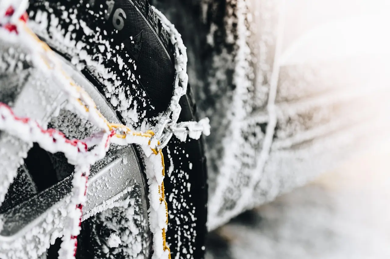 Modern sedan in snow while a driver checks tire chain fitment near the front wheel
