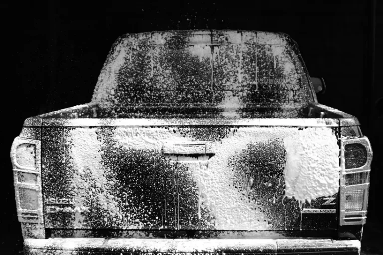 Car cleaner products beside microfiber towels next to a dusty SUV in natural daylight
