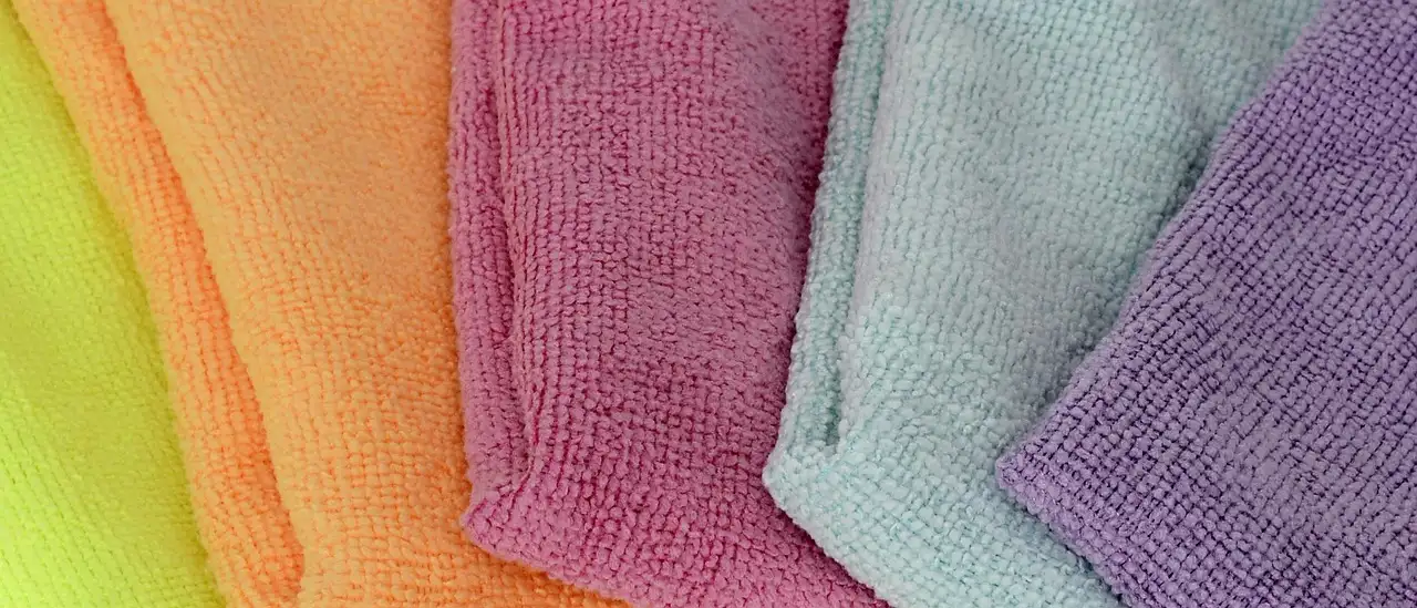 Three car cleaning cloth sets on a garage workbench beside a silver sedan.