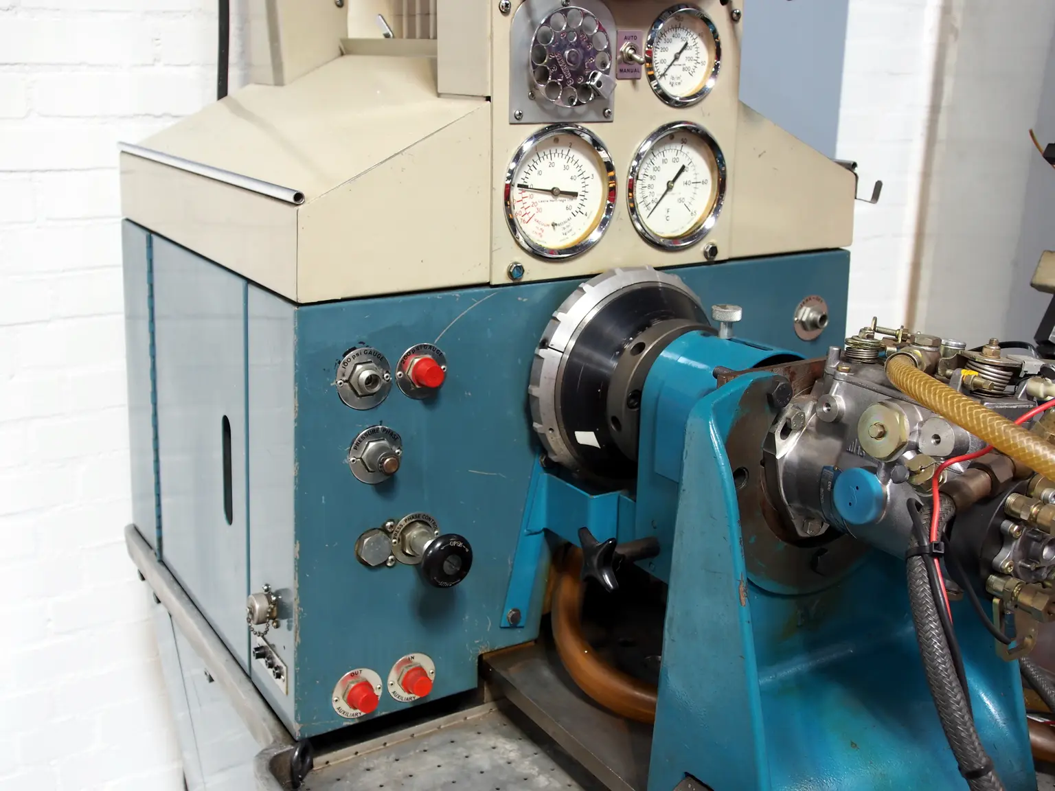 Close-up of a fuel pump test setup with hoses, wiring, multimeter, and fuel sample bottle