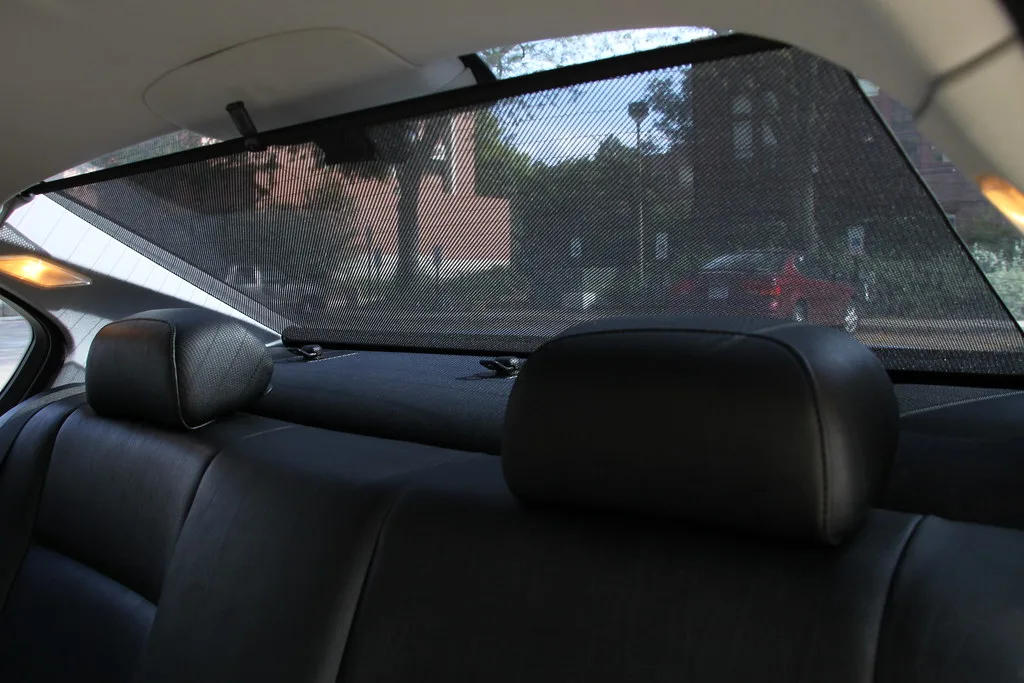 Hands adjusting a car seat sun shade around a rear-facing car seat and window edge