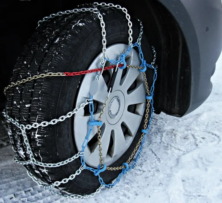 Driver fitting car snow chains beside a compact SUV on a snowy mountain roadside