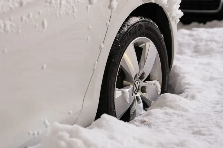 Driver comparing winter tire tread patterns beside a snow-dusted SUV on a frosty street