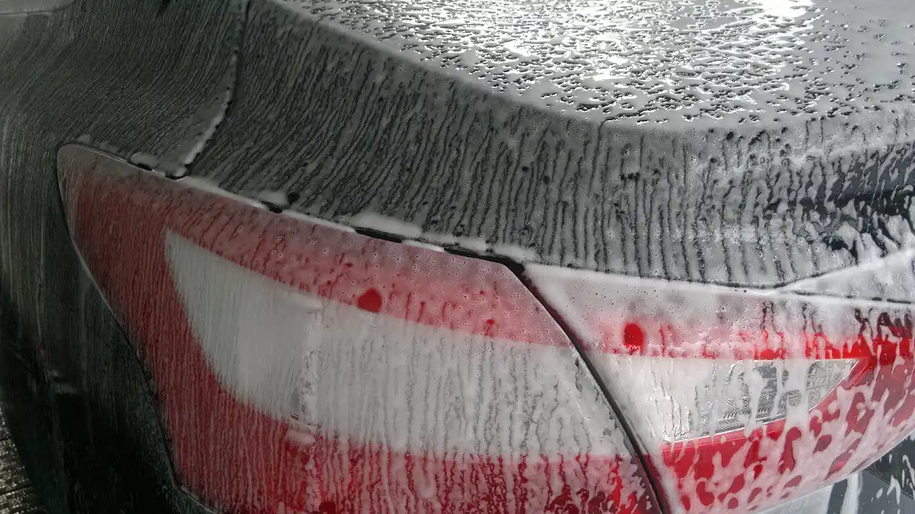 Detailer comparing car wax and sealant beside a freshly polished dark sedan in natural light
