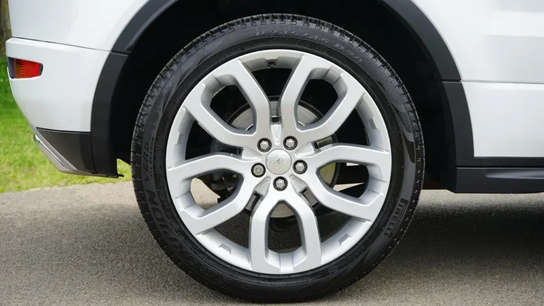 Car wheels and rims lined up in a sunlit auto shop with a sports car in the background