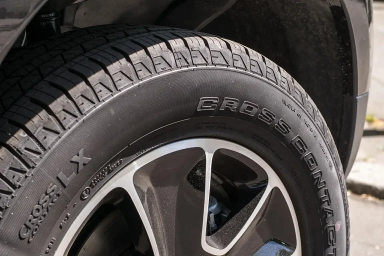 Detailer comparing wheel cleaners beside a sedan with clean and dirty alloy wheels in natural light